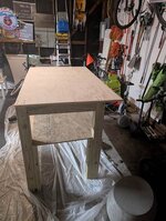 The image depicts a simple wooden workbench situated in a cluttered, colorful workshop setting, surrounded by tools and materials.  AI-generated content may be incorrect.